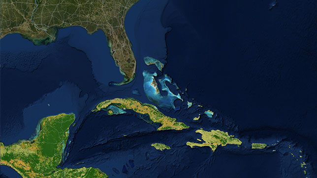 Uma área no Mar do Caribe com ilhas iluminadas em amarelo e verde, e algumas áreas de água perto de Florida Keys iluminadas em tons de azul mais brilhantes do que o oceano circundante